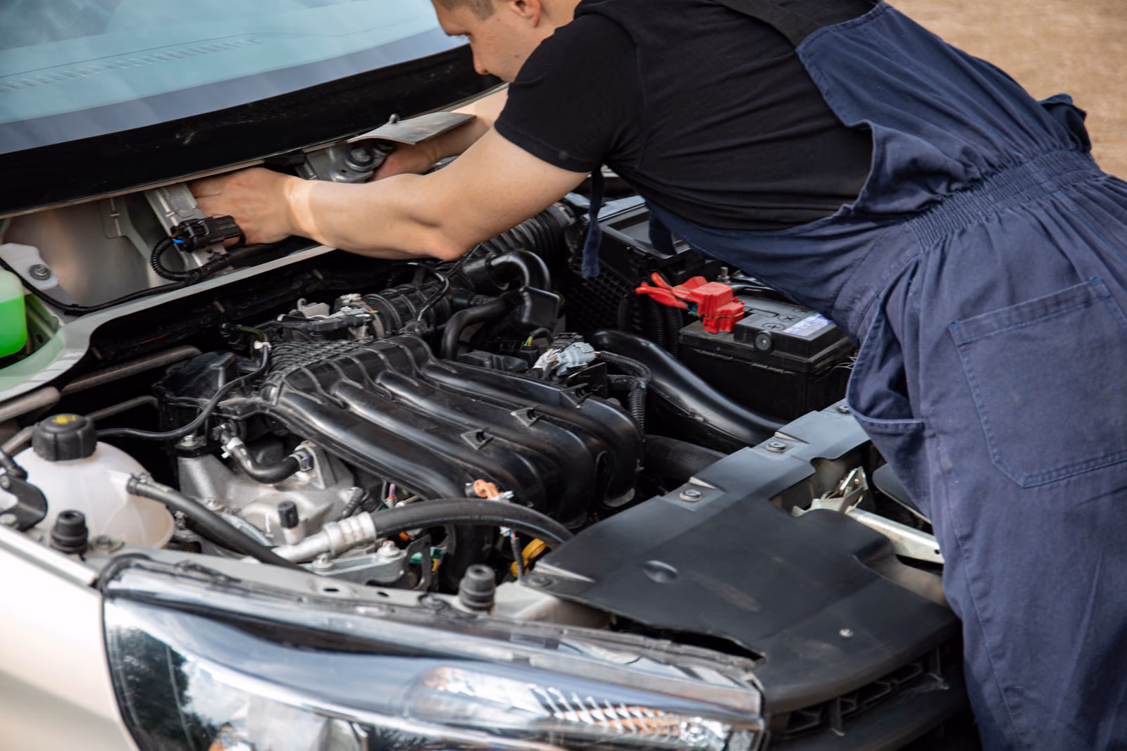 A mechanic working under the hood of a car outdoors